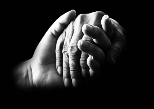 images shows two hands held together. Image is black and white on a black background.