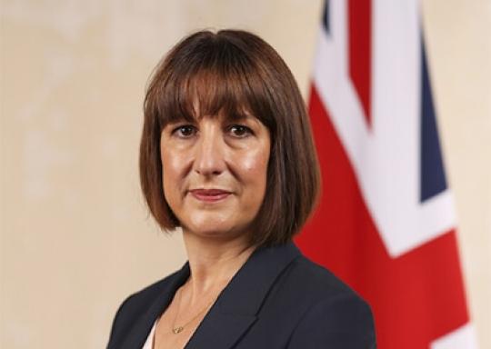 Rachel Reeves is stood in front of a union jack looking at the camera.