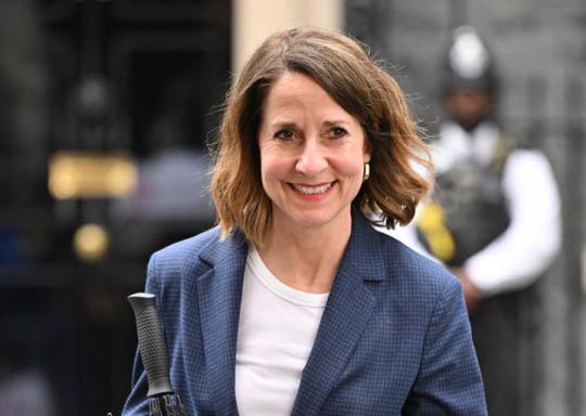 Image shows Liz Kendall MP smiling at the camera. She has shoulder length black hair and is wearing a blue blazer and a white shirt.