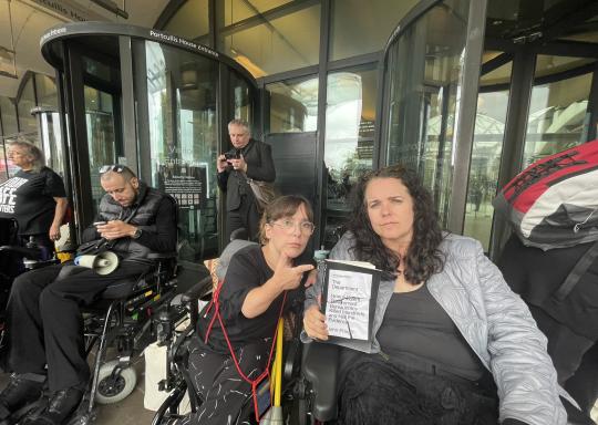 Photo of two people holding the department book and blocking portcullis house